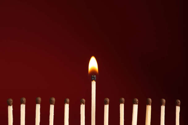 Burning match among unlit ones on red background, closeup - Φωτογραφία, εικόνα