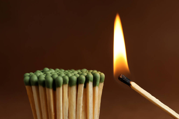 Burning match near unlit ones on brown background, closeup - Fotó, kép