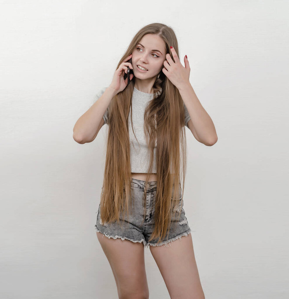 Young girl, long hair, denim shorts, talking on phone, funny conversation on the phone - Zdjęcie, obraz
