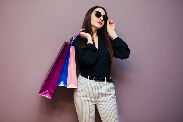Portrait of excited pretty girl in blouse and sunglasses holding shopping bags isolated on purple background. - Фото, зображення