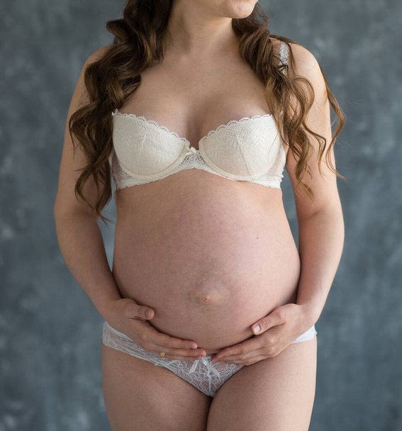 白い下着を着た妊娠中の美しい若い女性は彼女の腹を抱擁する。幸せな母親の概念は - 写真・画像