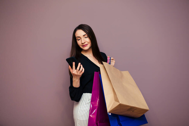 Beautiful well-dressed young girl holding a blank paper bag and shopping at an online store against a wall background with copy space for text or design. Horizontal layout. - Фото, изображение
