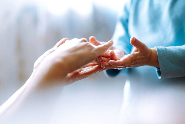 Мама допомагає гойдалці помити руки. Вони стирають руки разом, створюючи піну з милом. Гігієна концепція. Запобігти поширенню мікробів і бактерій і уникнути зараження коронавірусом.. - Фото, зображення