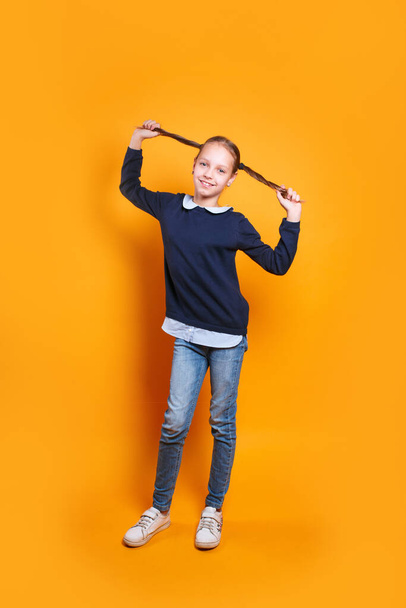 funny happy little girl in casual clothes having fun on yellow studio background - Foto, Imagen