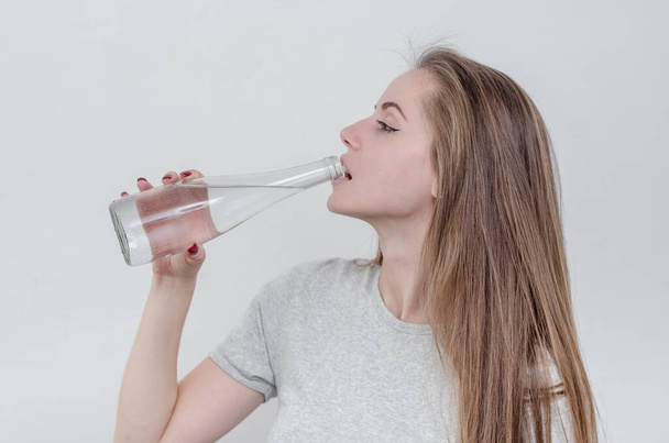 Красива дівчина з прозорою скляною пляшкою в руках. П'є воду з шиї пляшки
. - Фото, зображення