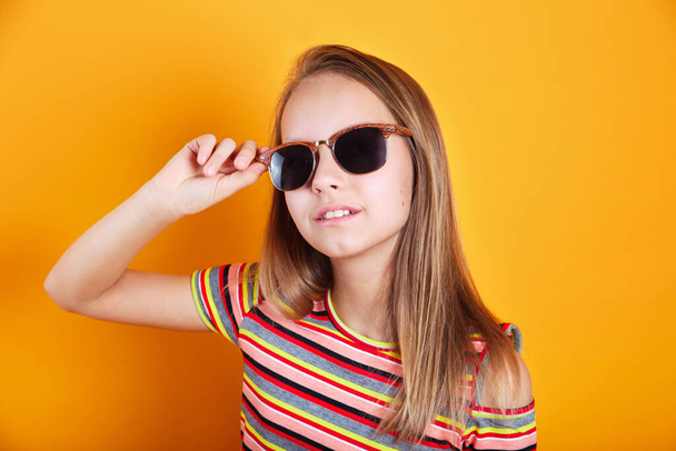 Close-up of trendy little girl in summer clothes and sunglasses on yellow background - 写真・画像