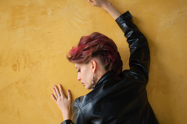 Zadní pohled na okouzlující dámu v punk rock stylu party oblečení s tmavými růžovými vlasy v ležérní šaty, černá kožená bunda, a dlouhé náušnice na žlutém pozadí - Fotografie, Obrázek