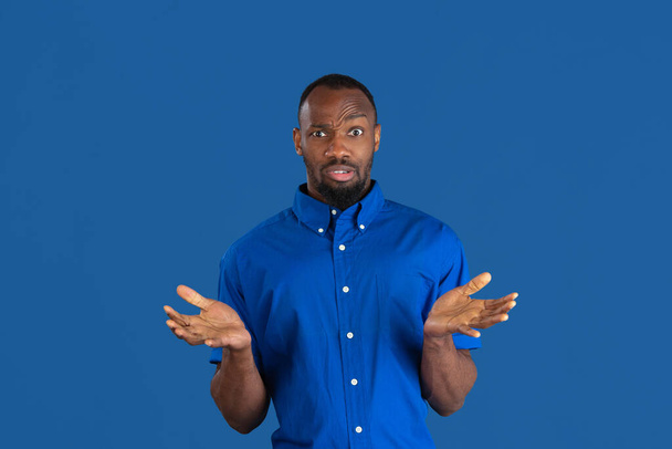 Monochrome portrait of young african-american man on blue studio background - 写真・画像