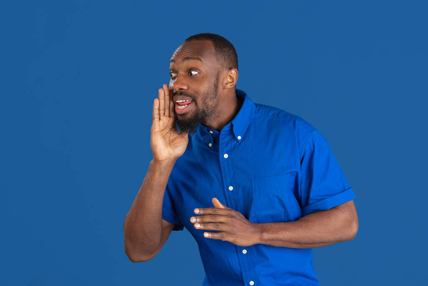Monochrome portrait of young african-american man on blue studio background - 写真・画像