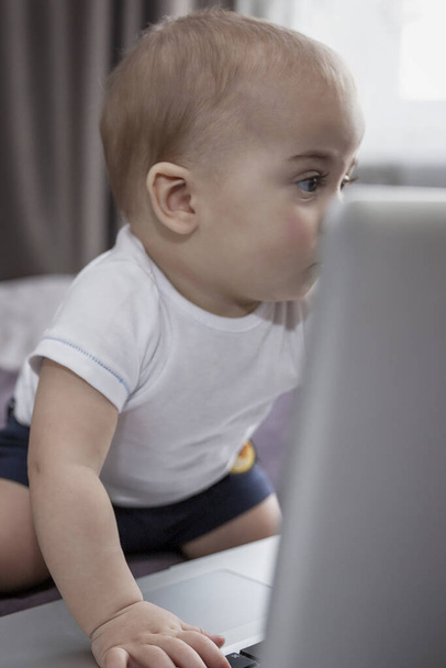 The baby looks with interest at the laptop screen. New generation. Close-up. Verttcal. - Fotoğraf, Görsel