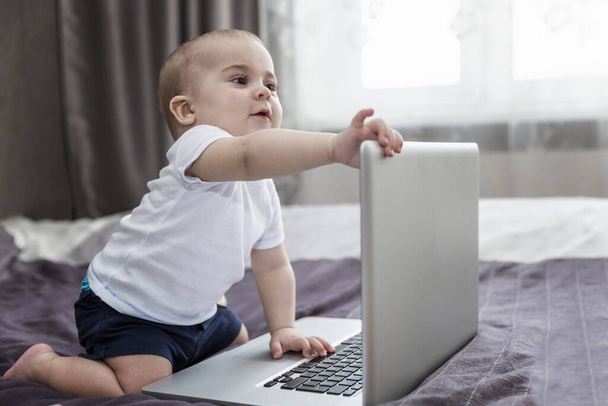 Baby is sitting on the bed with a laptop. New generation. - Foto, imagen