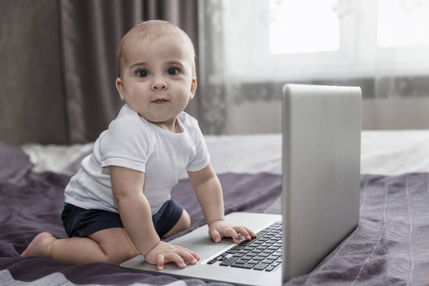Baby is sitting on the bed with a laptop. New generation. - Foto, Imagen