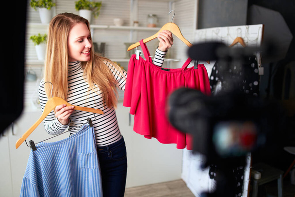 Fashion blogger woman in jeans and turtleneck showing casual colorful shirts on camera. Stylist influencer girl showing trendy clothes filming vlog episode for her channel. Opinion leader sets trends. - Photo, Image