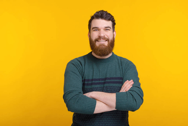 Smiling bearded man with arms crossed is looking at the camera over yellow background - Foto, Bild
