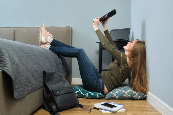 Fiatal nő egyetemi hallgató digitális táblagépet olvas, online oktatás, távoktatás. Okos lány szemüveggel ül a padlón - Fotó, kép
