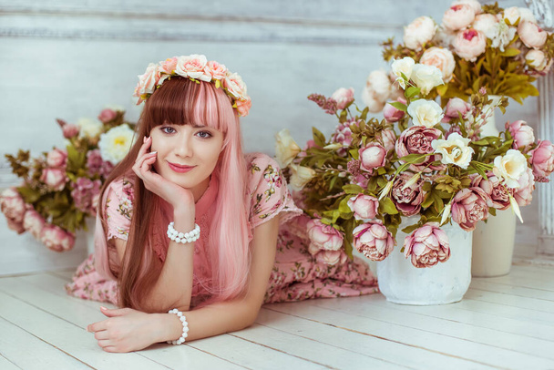 Beautiful young woman doll in a pink dress lies on the floor in a bright room and flowers, lolita. Japanese street fashion. Portrait. - Zdjęcie, obraz