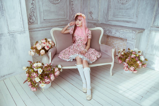 Beautiful young woman doll in a pink dress in a room with flowers, sitting on the couch, lolita. Japanese street fashion. - Foto, Imagen