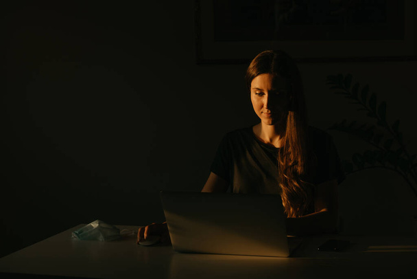 Une femme caucasienne étudiant à distance sur son ordinateur portable pendant la quarantaine pour éviter la propagation du coronavirus. Une femme d'affaires travaillant à domicile le soir pendant la pandémie de COVID-19
. - Photo, image