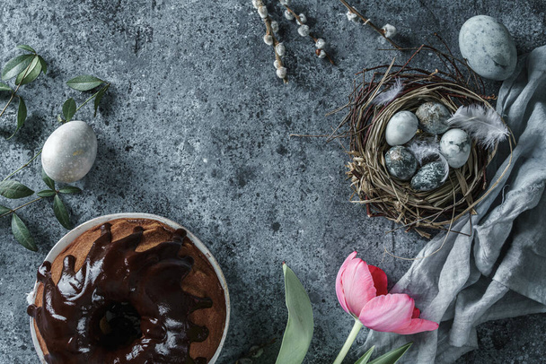Vrolijke paasvakantie compositie met paaseieren in nest, paastaart en lente tulpen bloemen op blauwe achtergrond. Bovenaanzicht, vlak lay - Foto, afbeelding