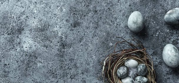 Мраморные пасхальные яйца в птичьем гнезде с перьями и весенними цветами на синем фоне с салфеткой. С праздником Пасхи, вид сверху, плоская постель
 - Фото, изображение
