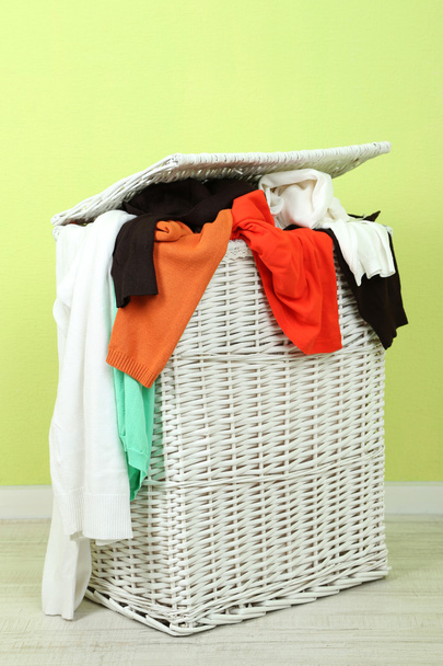 Full laundry basket on wooden floor on green wall background - Foto, immagini