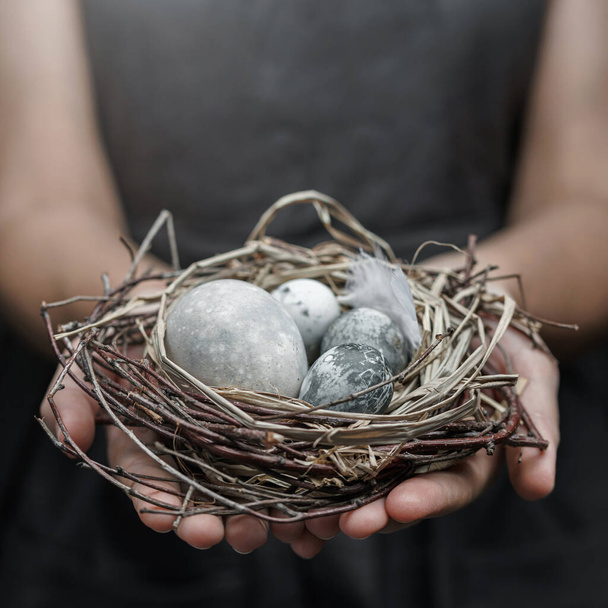 Ženské ruce drží mramorová velikonoční vajíčka s peřím na tmavém pozadí. Veselé Velikonoce, selektivní zaměření - Fotografie, Obrázek