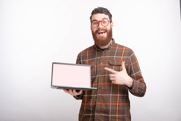 Spójrz na tę ofertę lub baner na czystym ekranie mojego laptopa. Brodaty mężczyzna trzyma komputer na białym tle. - Zdjęcie, obraz