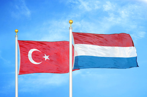 Τουρκία και Ολλανδία δύο σημαίες σε κοντάρια σημαίας και φόντο μπλε συννεφιασμένο ουρανό - Φωτογραφία, εικόνα