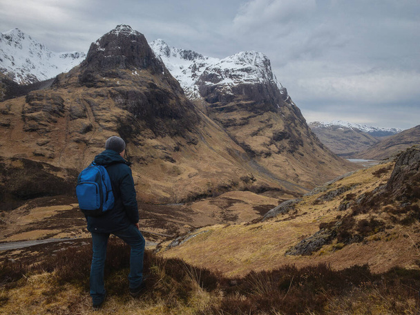 Man hiker with a backpack on the mountain from the back, looking at the mountain valley. The concept of active relaxation, motivation and goal achievement. Glencoe, Scotland, UK. - Фото, изображение