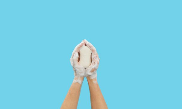 Kézhigiéniai fogalom. A női kezekben antibakteriális szappan van, habbal a kék háttéren. Kézfertőtlenítő a coronovírus pandémia alatt - Fotó, kép