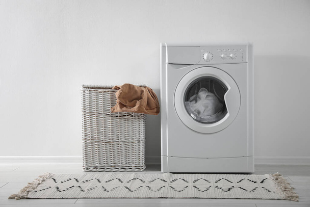 Modern washing machine and laundry basket near white wall indoors. Bathroom interior - Фото, зображення