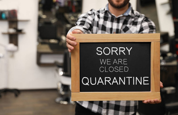 Business owner holding sign with text SORRY WE ARE CLOSED QUARANTINE in barber shop, closeup - Foto, Imagem