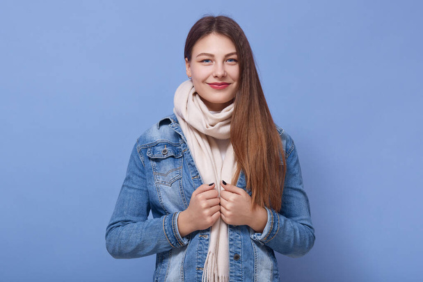 Close up portrait of happy woman wearing denim jacket and scarf, posing isoalted over blue background, lady with positive facial expression, attractive girl looking directly at camera. People concept. - Photo, image