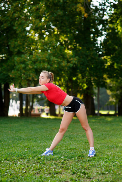 A young blonde girl is engaged in sports in the park, a woman does a warm-up in the street. Active outdoor training  - Foto, immagini