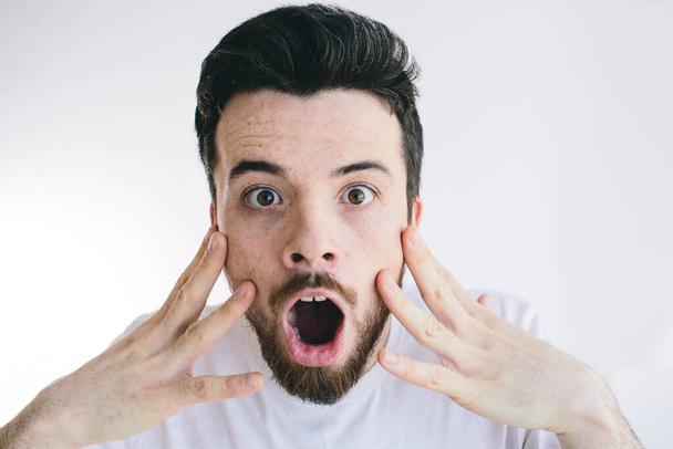 Man with shocked, amazed face expression look straight on camera. Hold fingers on cheeks with opened mouth. Isolated over white background. - 写真・画像
