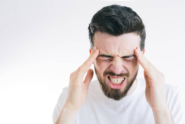 Picture of young bearded brunette man suffer from strong pain or headache. Hold fingers close to side of head. Need pill or medicine for relief. Isolated over background. - Фото, зображення