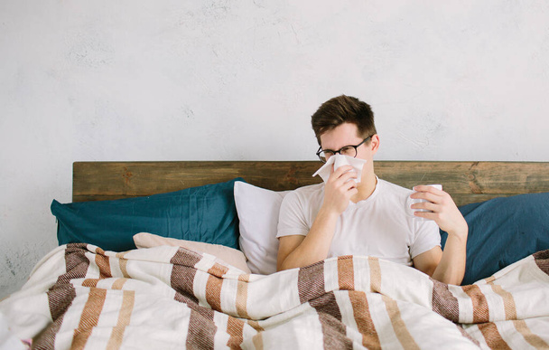 young man with handkerchief. Sick guy on the bed has runny nose. man makes a cure for the common cold - Foto, imagen