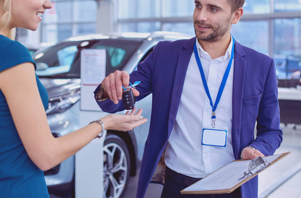 Car salesman sells a car to happy customer in car dealership and hands over the keys - Fotoğraf, Görsel