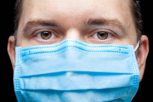 Male portrait a close up of a face with a serious expression in a blue medical mask isolated on a black background on a pulmonologist medical theme. - Fotografie, Obrázek