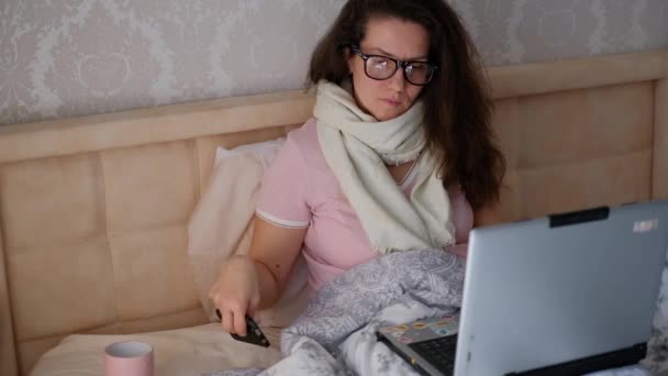 Sick woman in bed working on a laptop and talking on the phone. Self-isolation, work at home during a viral infection. - Filmagem, Vídeo