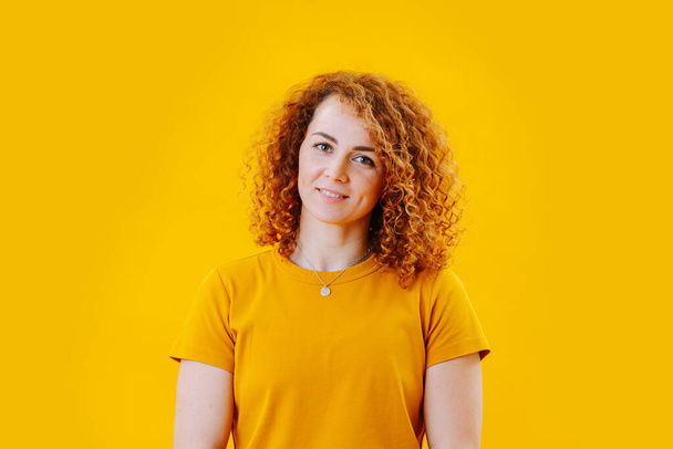 Kızıl saçlı, kıvırcık, sarı tişörtlü hoş bir kız. Sarı arkaplanda yakın plan portre - Fotoğraf, Görsel