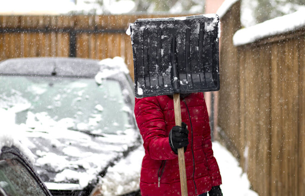 woman in red jacket with shovel cleaning snow. Winter shoveling. Removing snow after blizzard - Photo, Image