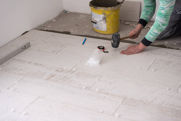 кваліфікований працівник встановлює керамічну дерев'яну плитку на підлогу Працівник робить ламінат на будівельному майданчику нової квартири
 - Фото, зображення
