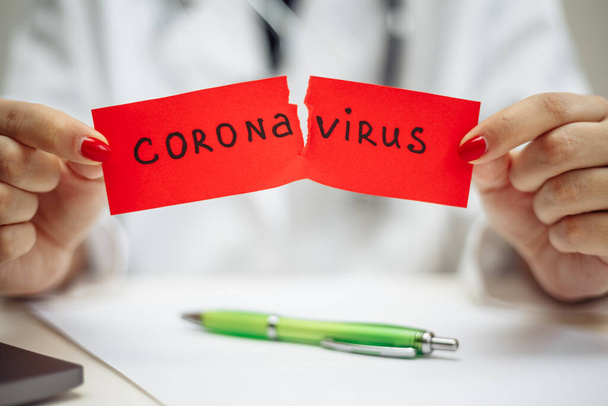 Ärztin mit OP-Maske zerreißt ein rotes Papier mit Mesaage Coronavirus, isoliert auf grauem Hintergrund. Krankenschwester mit nCov2019-Schild. Covid-19 und Krankheitsvorbeugekonzept - Foto, Bild