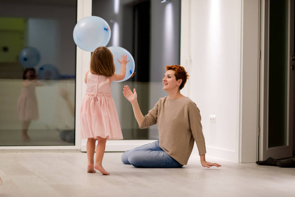 happy family spending time together young redhead mother and cute little daughter having fun while playing with balloons near the window on beautiful evening at home - Foto, imagen