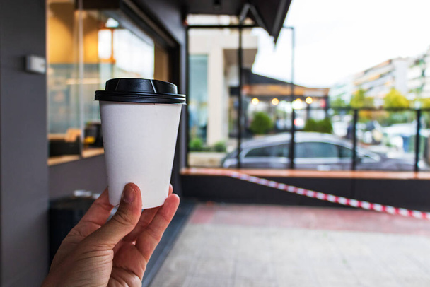 Male hand holding a take away coffee bought at a coffee shop without tables after Greek lockdown. - Photo, Image