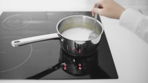 De koemelk kookt in een pan. Vrouw roert melk in steelpan - Video