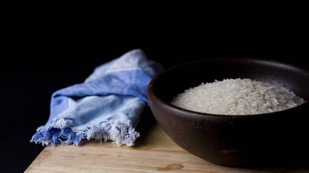 Niegotowany ryż w glinianej misce na drewnianym stole z czarnym tłem. - Zdjęcie, obraz