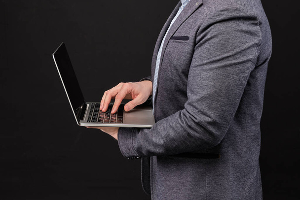 A man in a jacket works on laptop on a black background. Close up. - Foto, Imagem