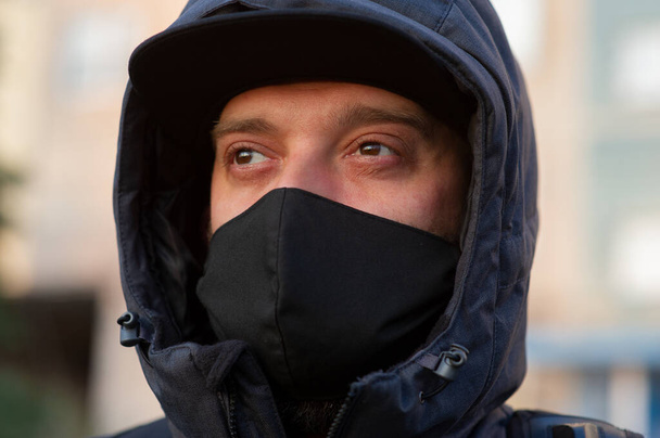 Un hombre con una máscara respiratoria negra en la cara. Un hombre en la calle con una máscara negra. Virus. Coronavirus. Un tipo en la primavera en la calle con una máscara respiratoria para protegerse contra el virus de la infección
 - Foto, imagen